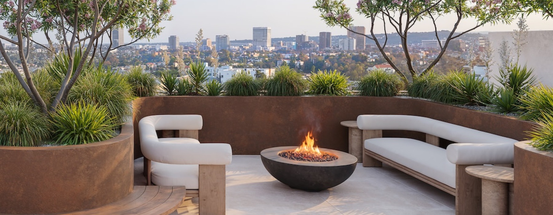a patio with a fire pit and a tree with flowers and a city in the background
